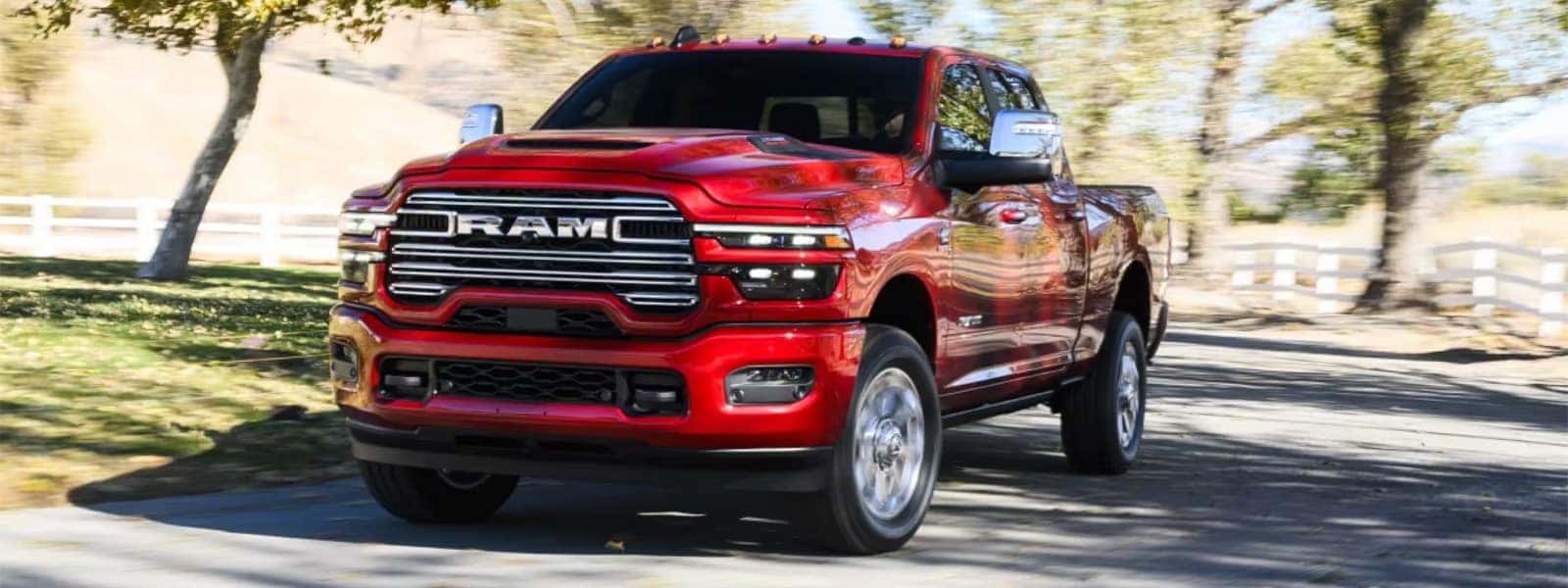 Red 2026 RAM 2500 heavy duty pickup driving on a country road with chrome grille and LED headlights