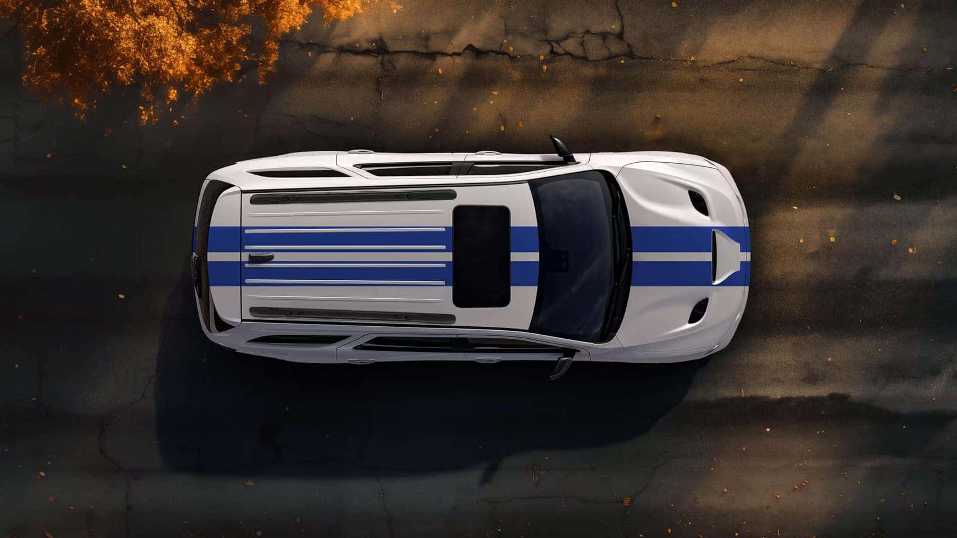 Top-down view of a white 2026 Dodge Durango with dual racing stripes and panoramic sunroof parked on a paved surface.