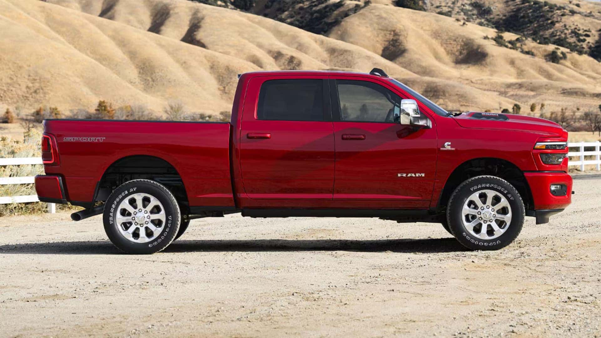 Side profile of a red 2026 RAM 2500 heavy duty truck parked outdoors showing long bed, crew cab, and Cummins diesel badge
