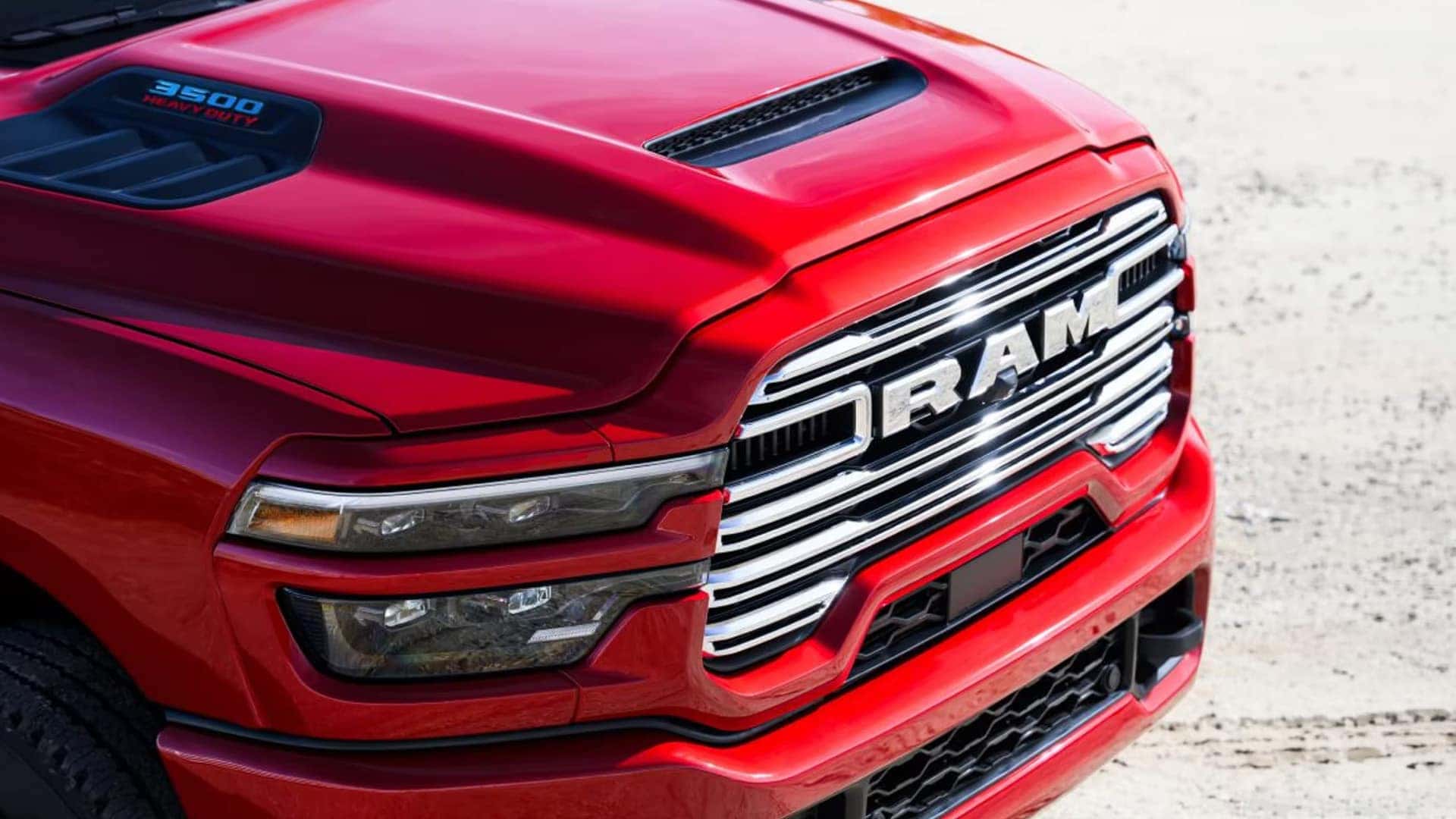 Front close up of red 2026 RAM 3500 showing bold RAM grille, hood scoop, and LED headlamps