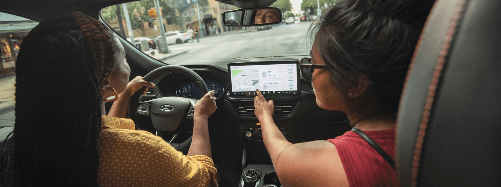 Two occupants in 2026 Ford Escape cabin as passenger points to center touchscreen with map and tiles