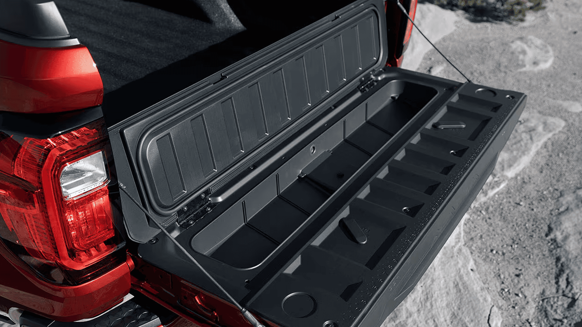 Open MultiStow tailgate storage compartment on a red 2026 GMC Canyon showing molded gear bins and drain channel.