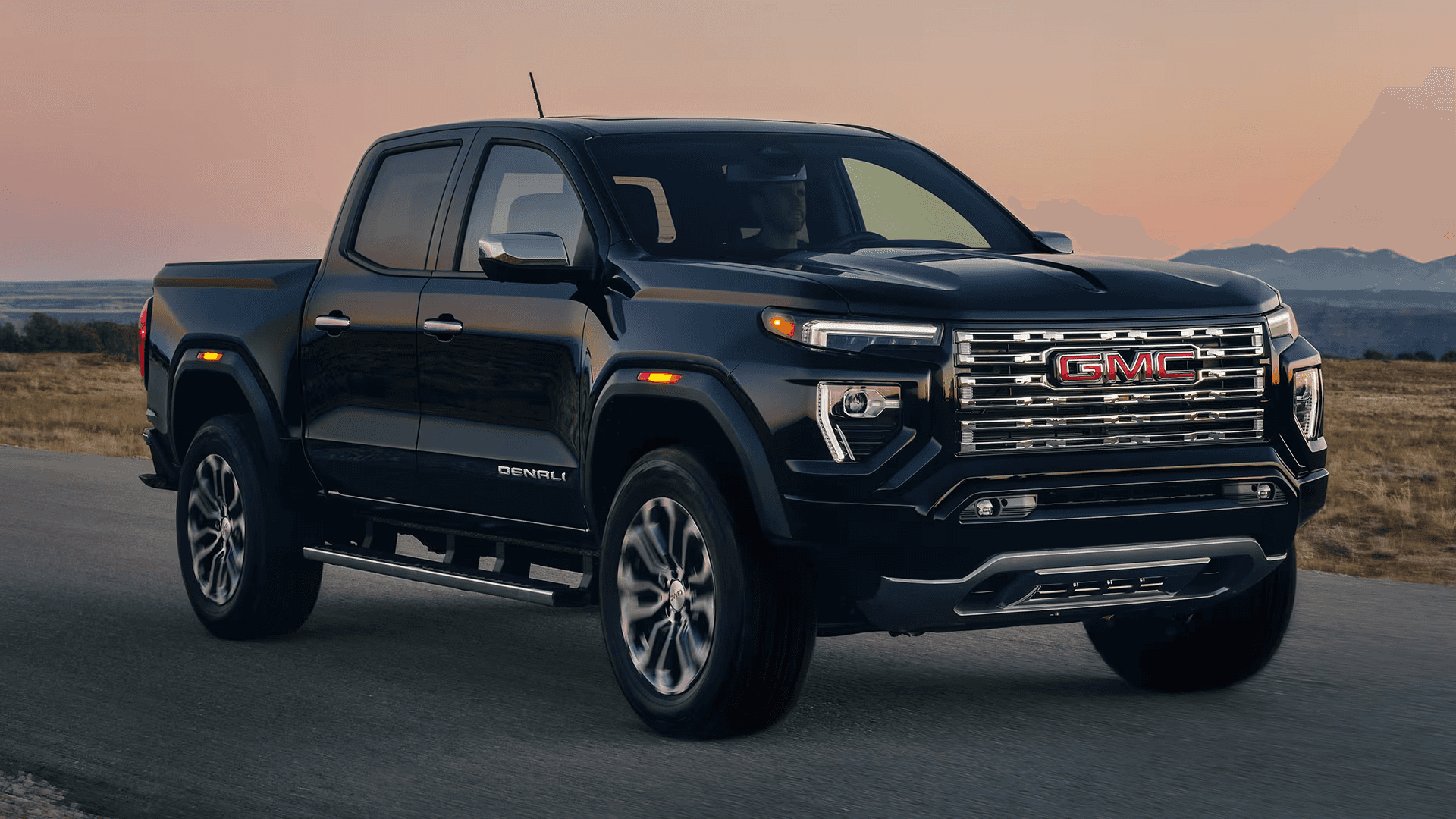 Black GMC Canyon Denali driving on an open road at sunset with chrome grille and LED lighting visible