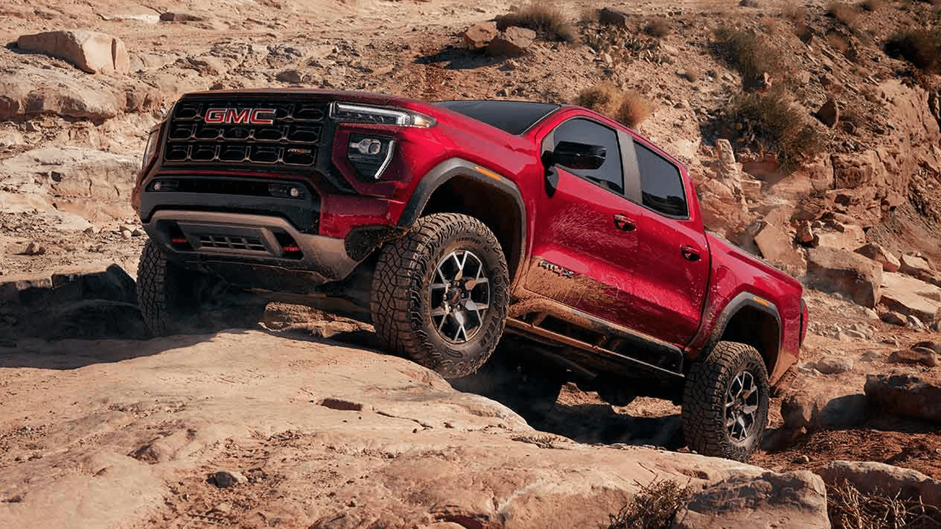 Red GMC Canyon AT4X climbing over rock ledges in desert terrain with off road tires and wide stance