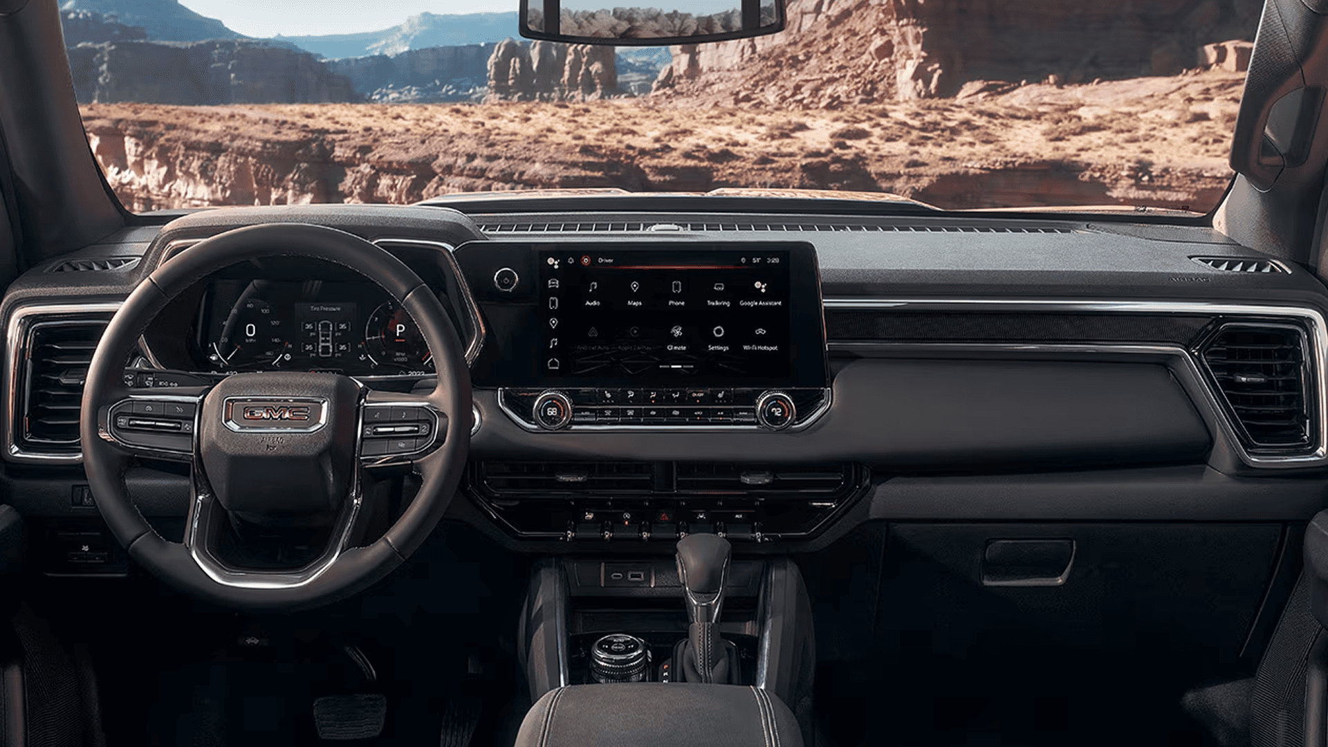 Front cabin view of the 2026 GMC Canyon showing the steering wheel, digital gauges, wide infotainment screen, and dashboard layout