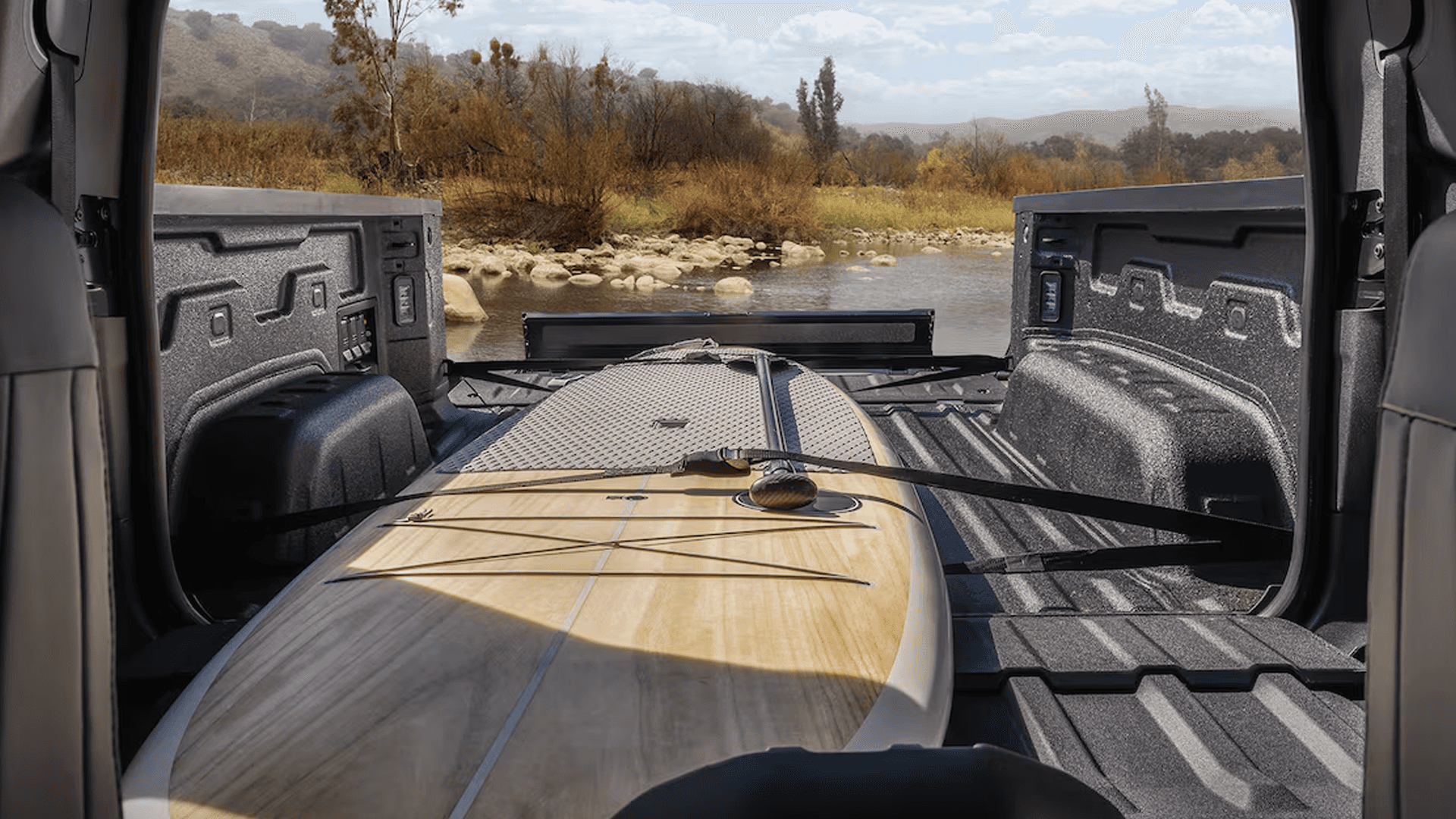 View from inside the cabin through the open truck bed and midgate, with a surfboard strapped in place