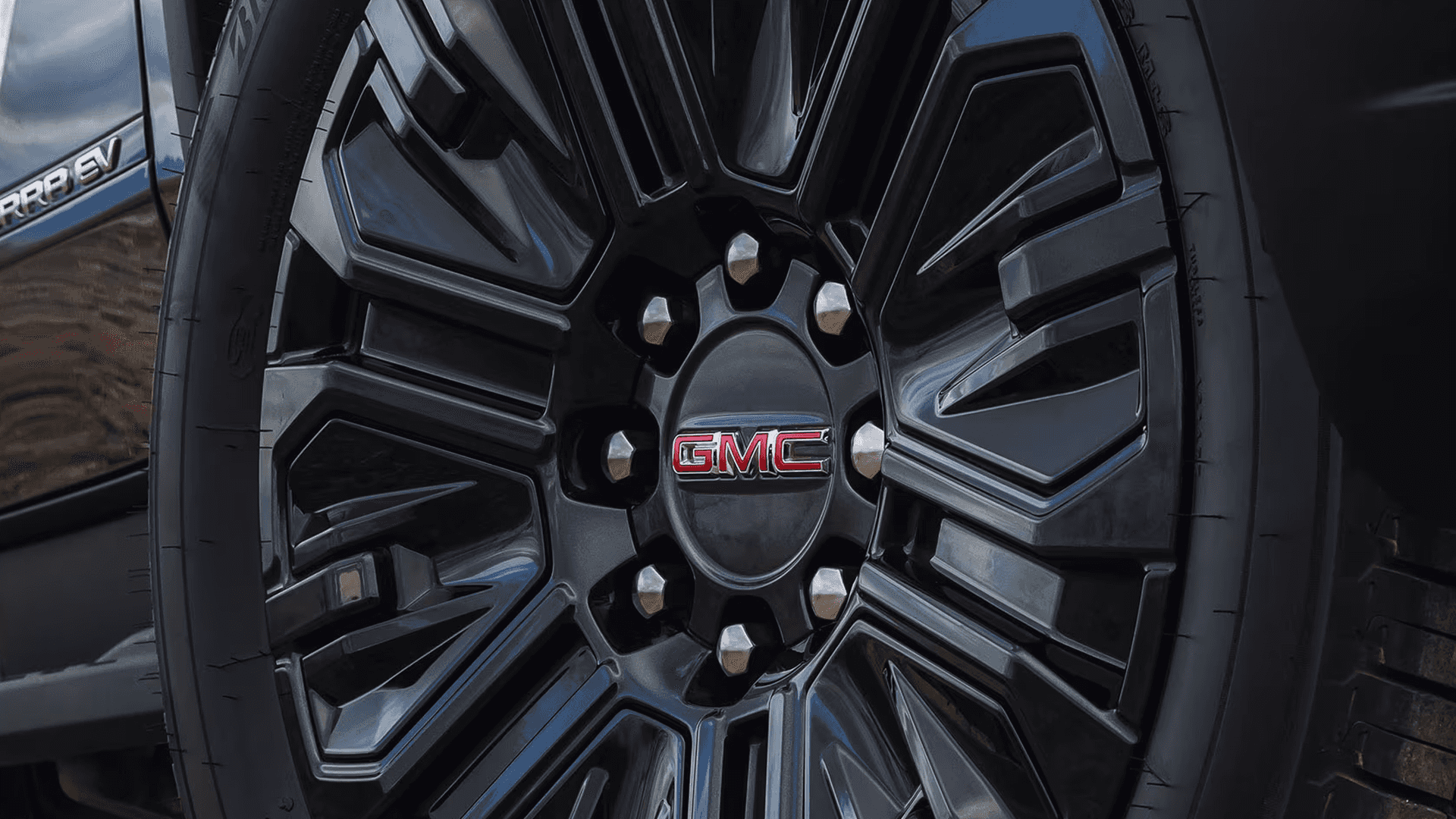 Close-up of a black GMC Sierra EV wheel with machined accents and a red GMC logo at the center cap
