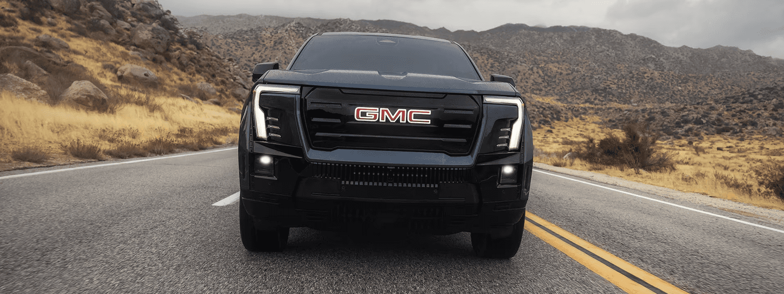 Black GMC Sierra EV shown head-on on a two-lane road with illuminated front badge and vertical LED lighting