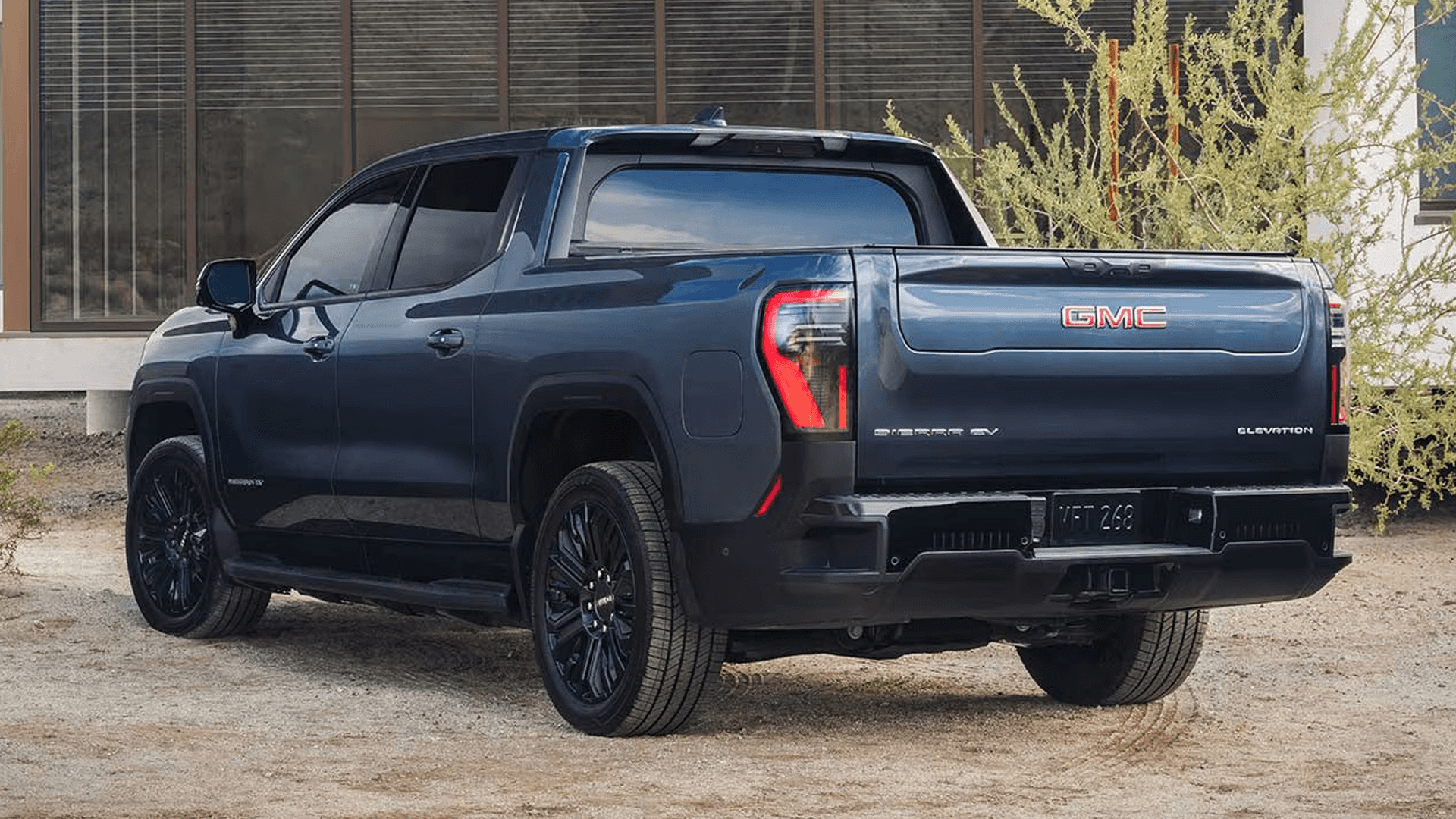 Rear three quarter view of blue GMC Sierra EV parked outside a building with taillights visible