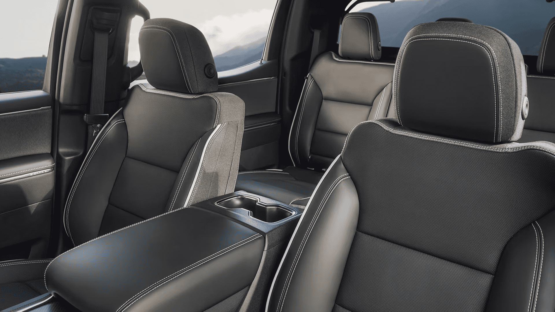 Black front seats and center armrest with cupholder visible inside GMC Sierra EV cabin