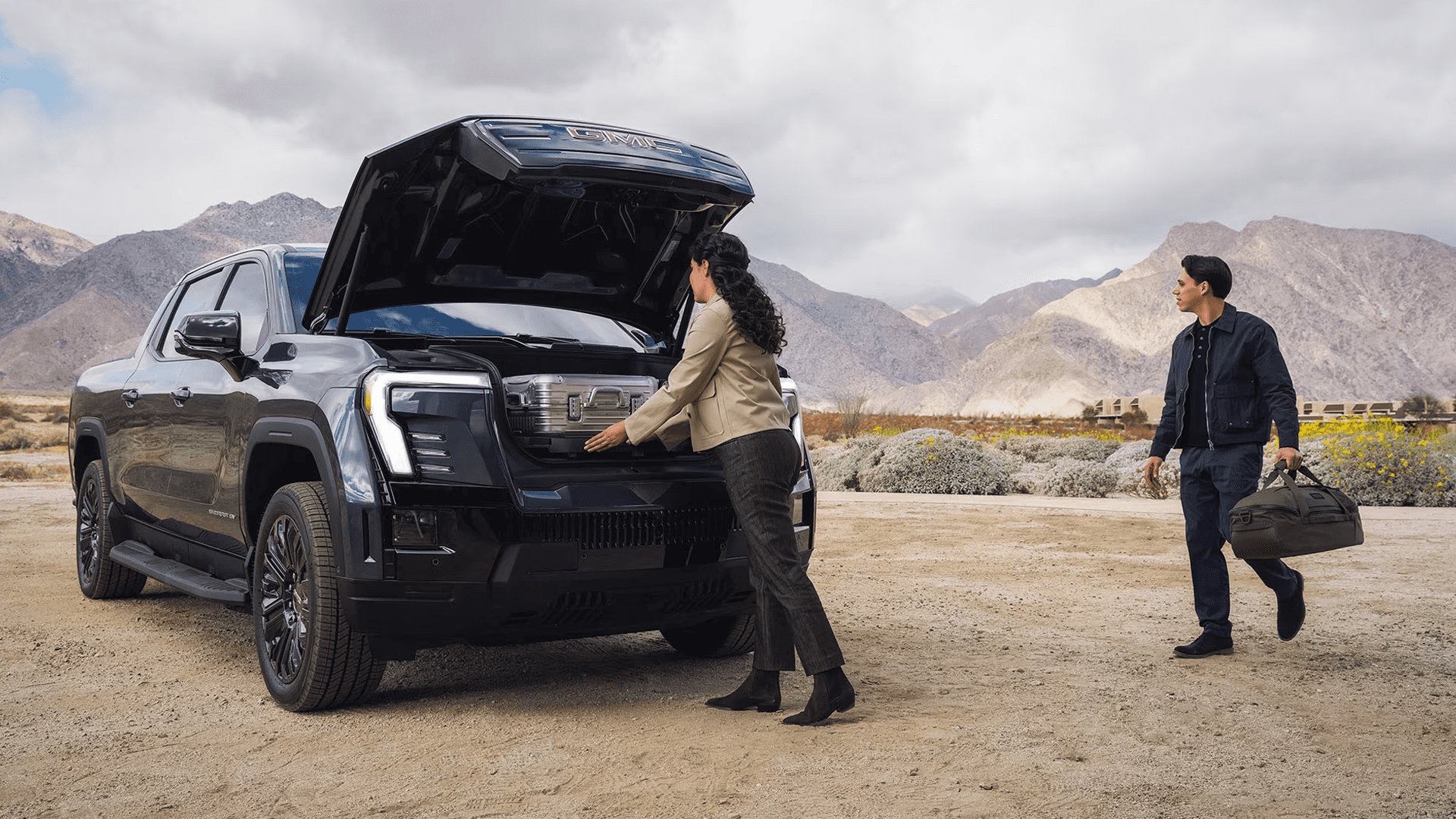Woman placing luggage in open front trunk of GMC Sierra EV as another person walks nearby