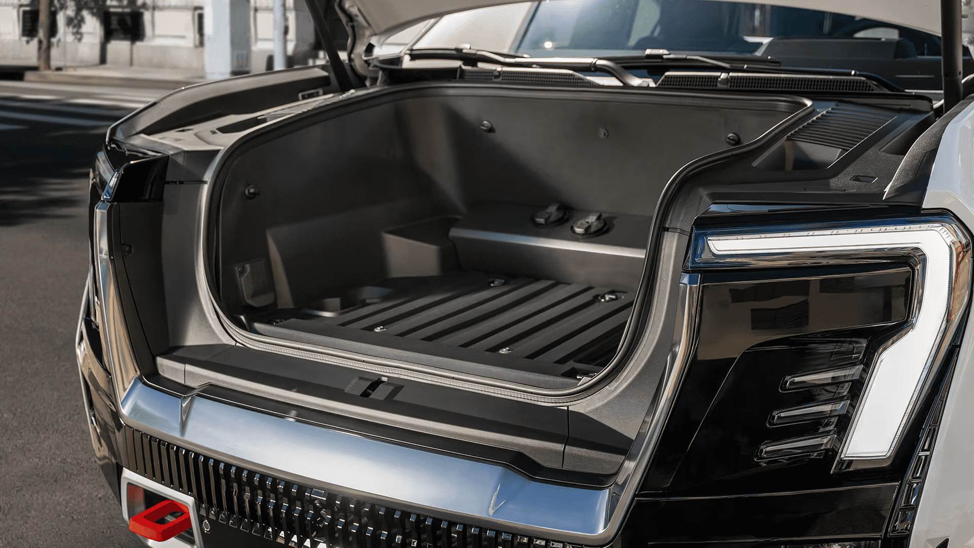 Open front cargo compartment on the GMC Sierra EV with molded side walls, ribbed floor, and hood raised