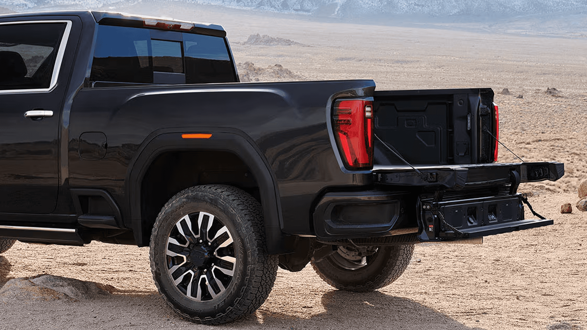 Rear three-quarter view of a GMC Sierra HD with the MultiPro Tailgate open in a desert landscape near mountains.
