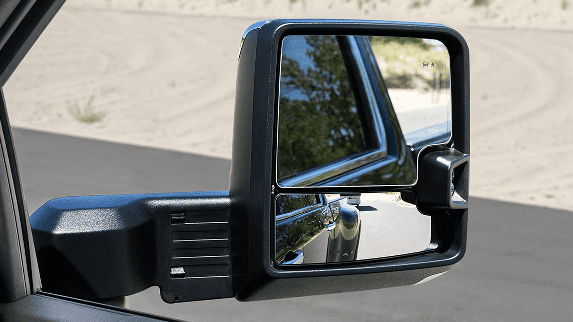 Close-up of a GMC Sierra HD trailering mirror with upper and lower glass reflecting the road and truck side.
