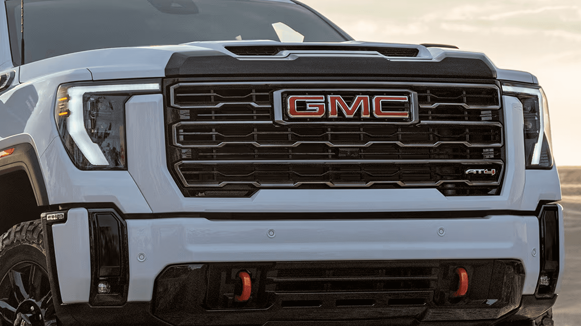 Front close-up of a white GMC Sierra HD AT4 grille with red recovery hooks and rugged trim-specific styling.