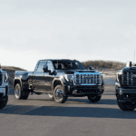 GMC Sierra HD lineup with AT4, dual rear wheel model, and Denali Ultimate parked in an open coastal setting