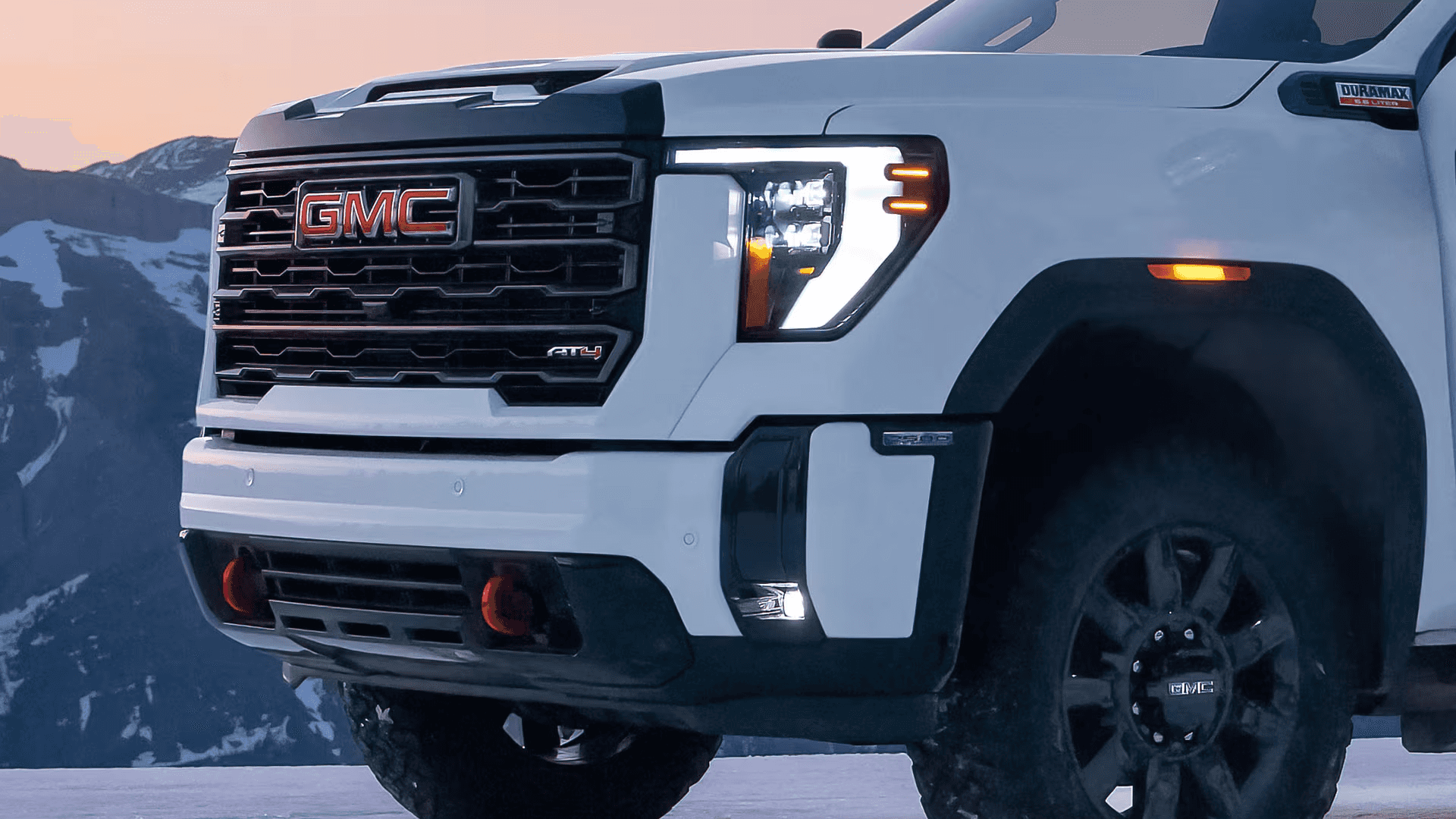 Close-up of the white 2026 GMC Sierra HD AT4 front end with Duramax badge, LED lighting, and red tow hooks.