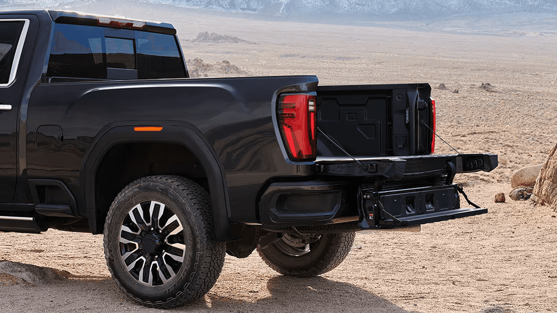 Black GMC Sierra HD with the MultiPro Tailgate open in the desert, highlighting bed access and cargo utility.