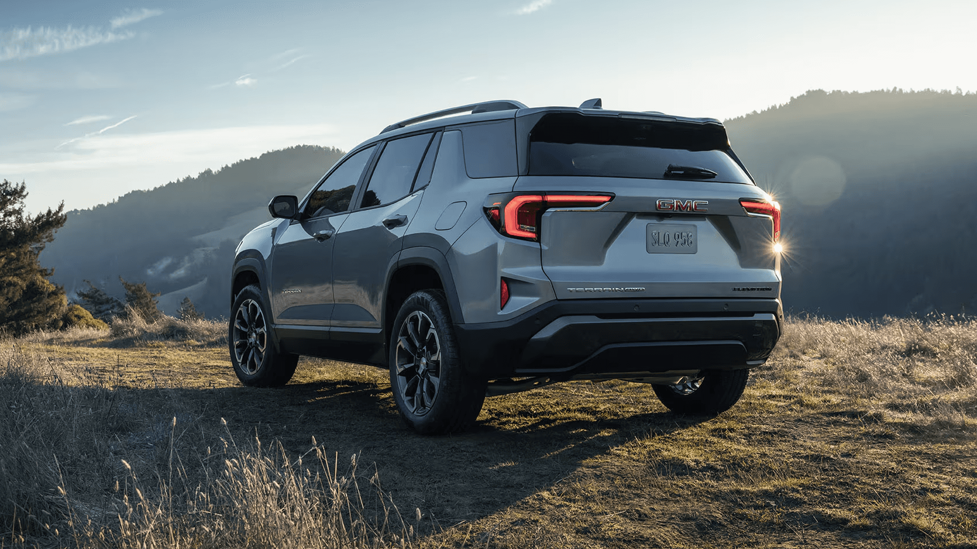 Rear view of silver GMC Terrain Elevation on grassy hill highlighting LED taillights and sculpted tailgate design.