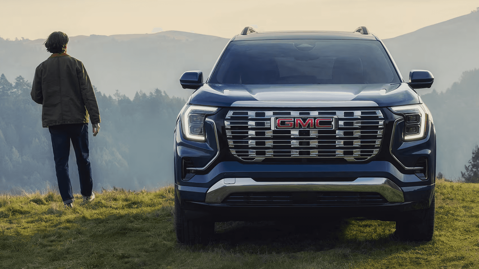 Front view of 2026 GMC Terrain Denali with bold chrome grille and signature LED lighting in mountain landscape.