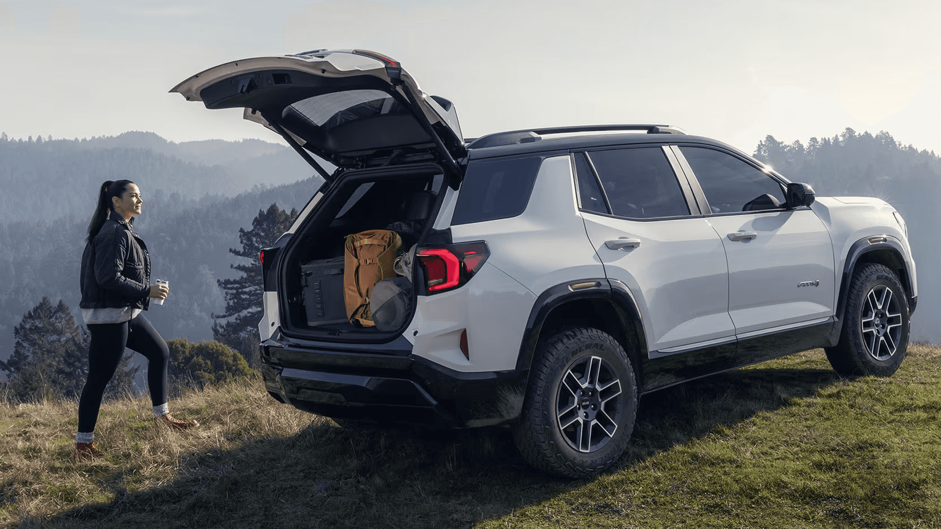 White GMC Terrain AT4 with power liftgate open showing cargo area and gear during outdoor adventure setting.