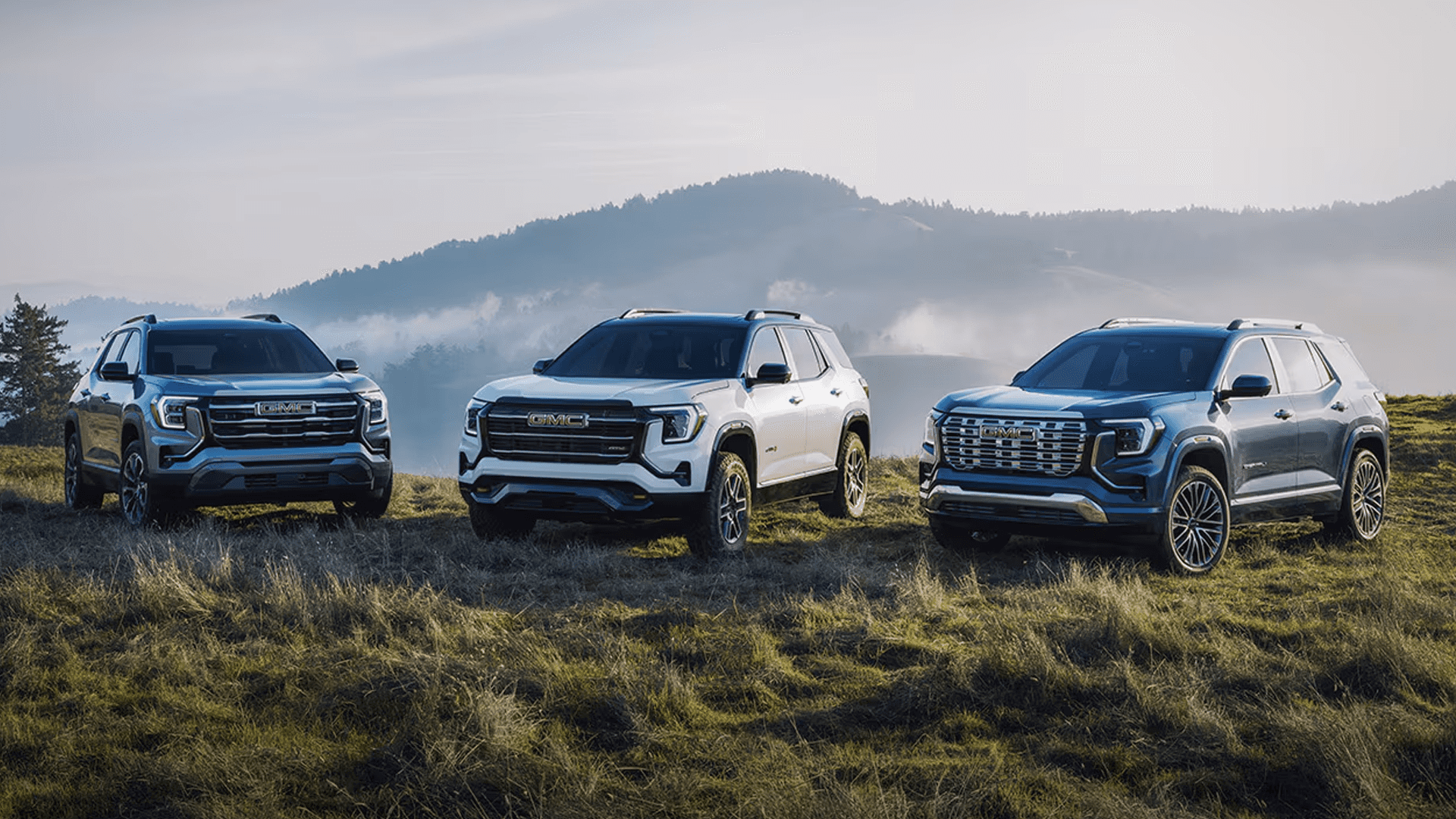 Three GMC Terrain SUVs displayed side by side on a grassy hillside highlighting different trim designs and styling.
