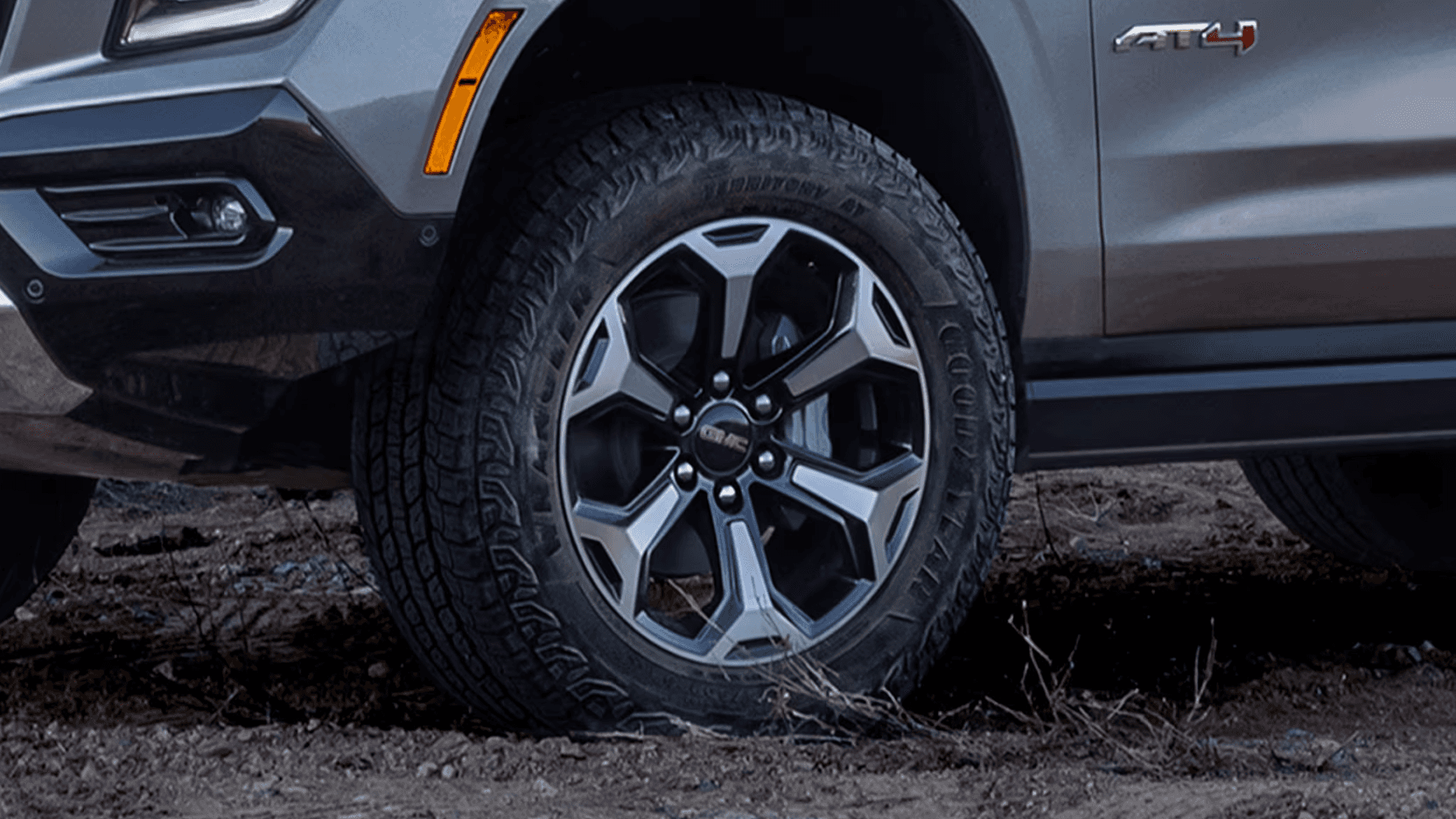 Close-up of a GMC Yukon AT4 front wheel with an all-terrain tire on rocky dirt ground.