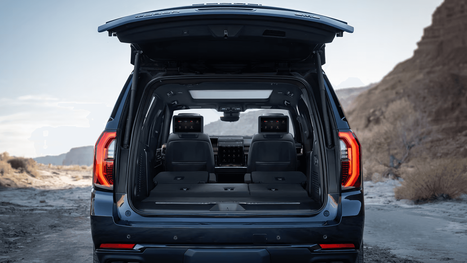 Rear view of a blue GMC Yukon with the liftgate open, showing the cargo area and folded rear seats.