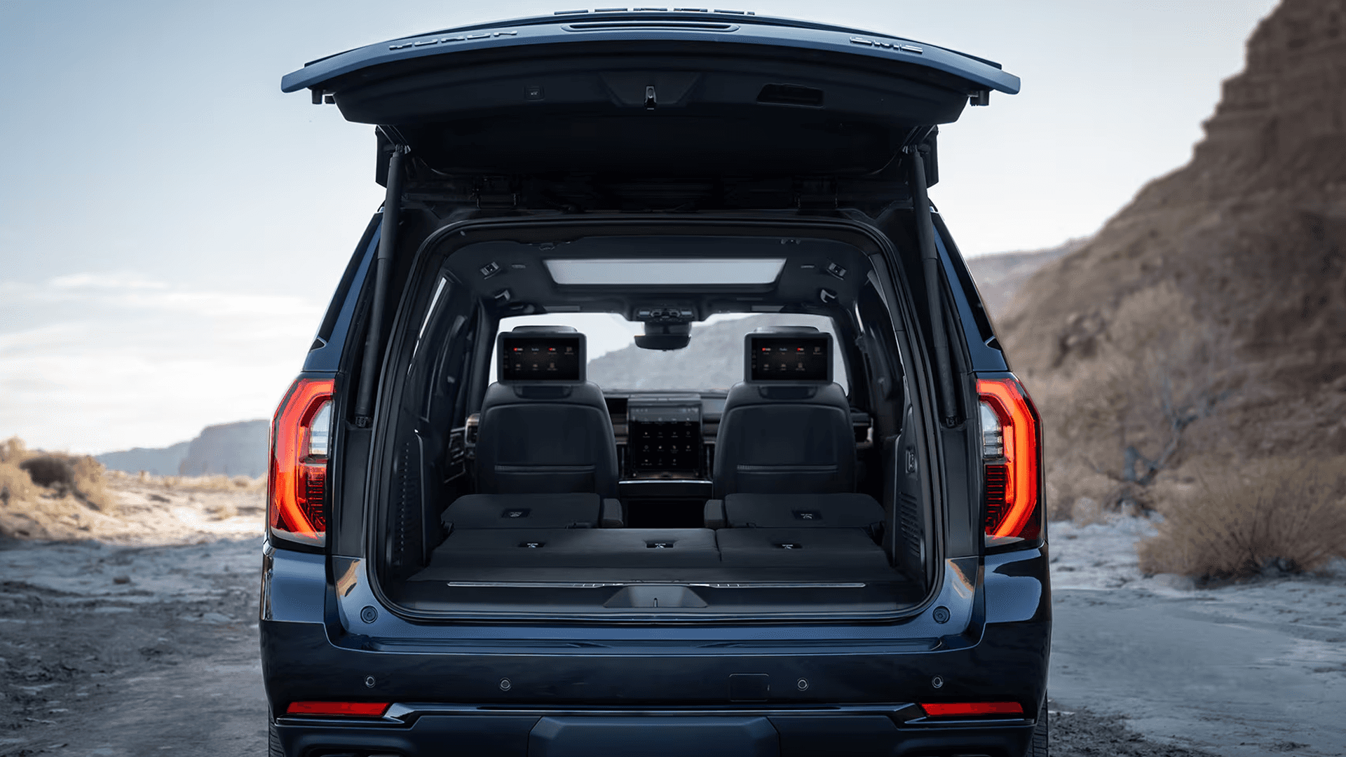 Rear view of SUV with liftgate open showing cargo area, folded rear seats, and rear seat screens in desert setting