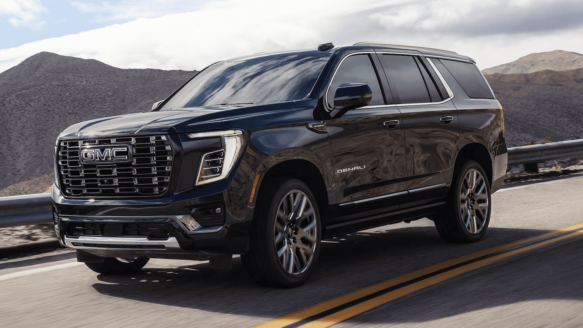 Front three quarter view of dark SUV driving on highway, showing large grille, LED headlights, and Denali badge