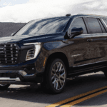 Dark blue GMC Yukon Denali driving on a desert highway with chrome grille, LED lighting, and mountain scenery