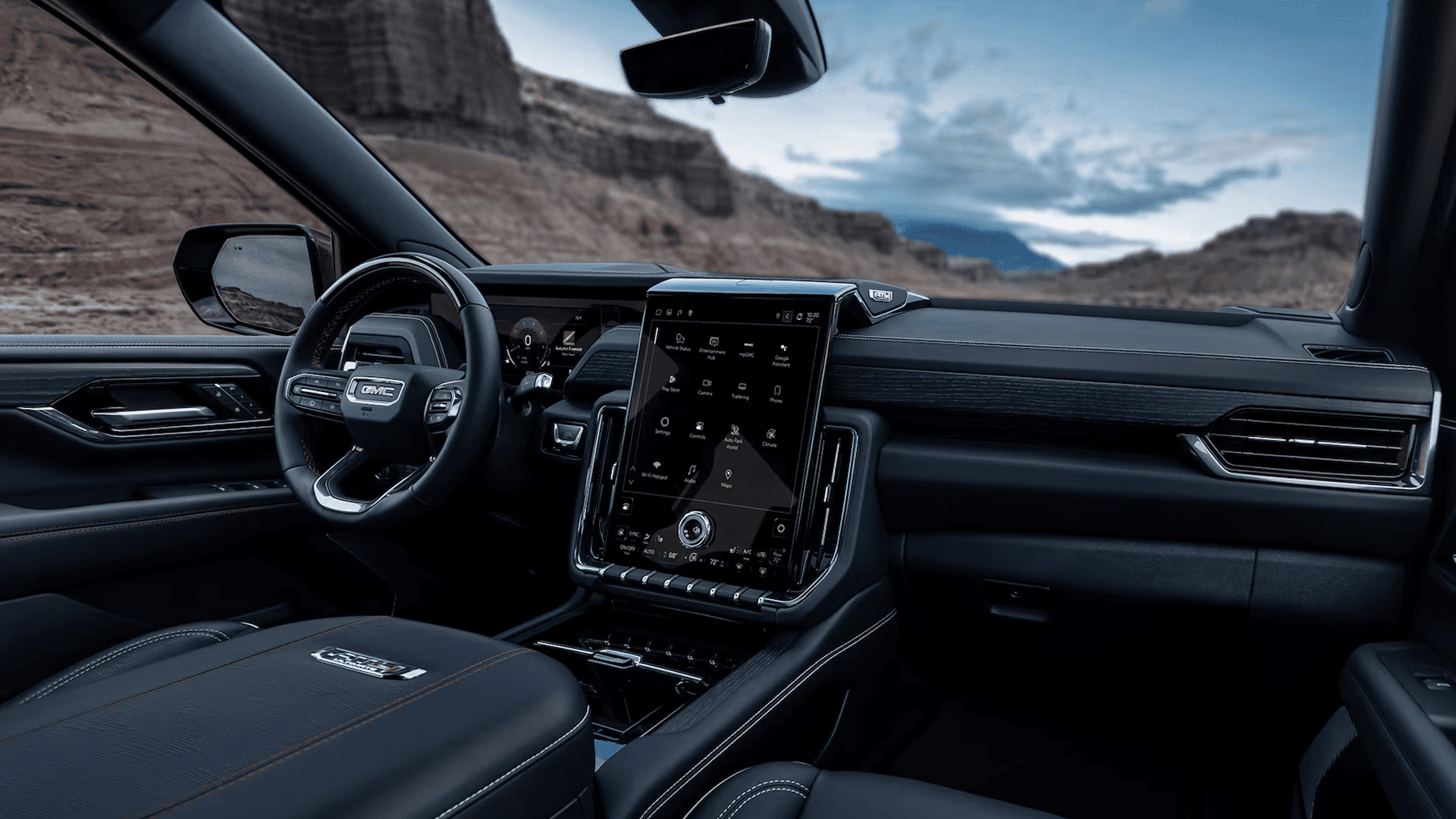 Black GMC Yukon cabin with tall touchscreen, leather-trimmed seats, steering wheel, and canyon view ahead