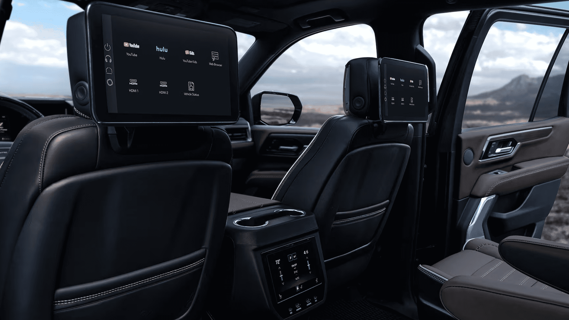 Rear GMC Yukon cabin with dual headrest screens, rear climate controls, captain’s chairs, and media apps shown