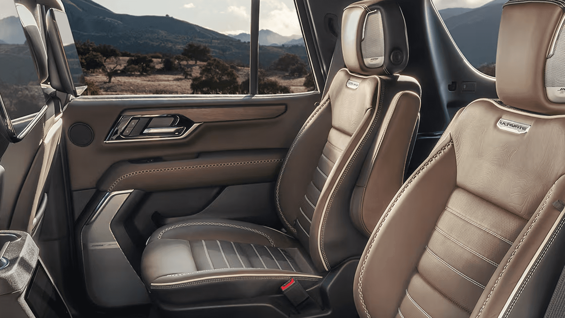 Second-row leather seats with visible stitching, door panel trim, window view of landscape, and integrated headrest speakers