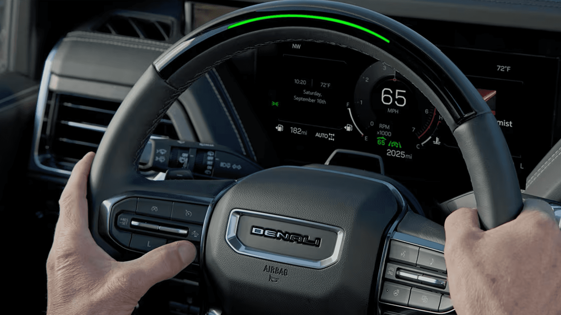 Driver holding steering wheel with illuminated light bar and digital gauge cluster displaying speed and driving info.