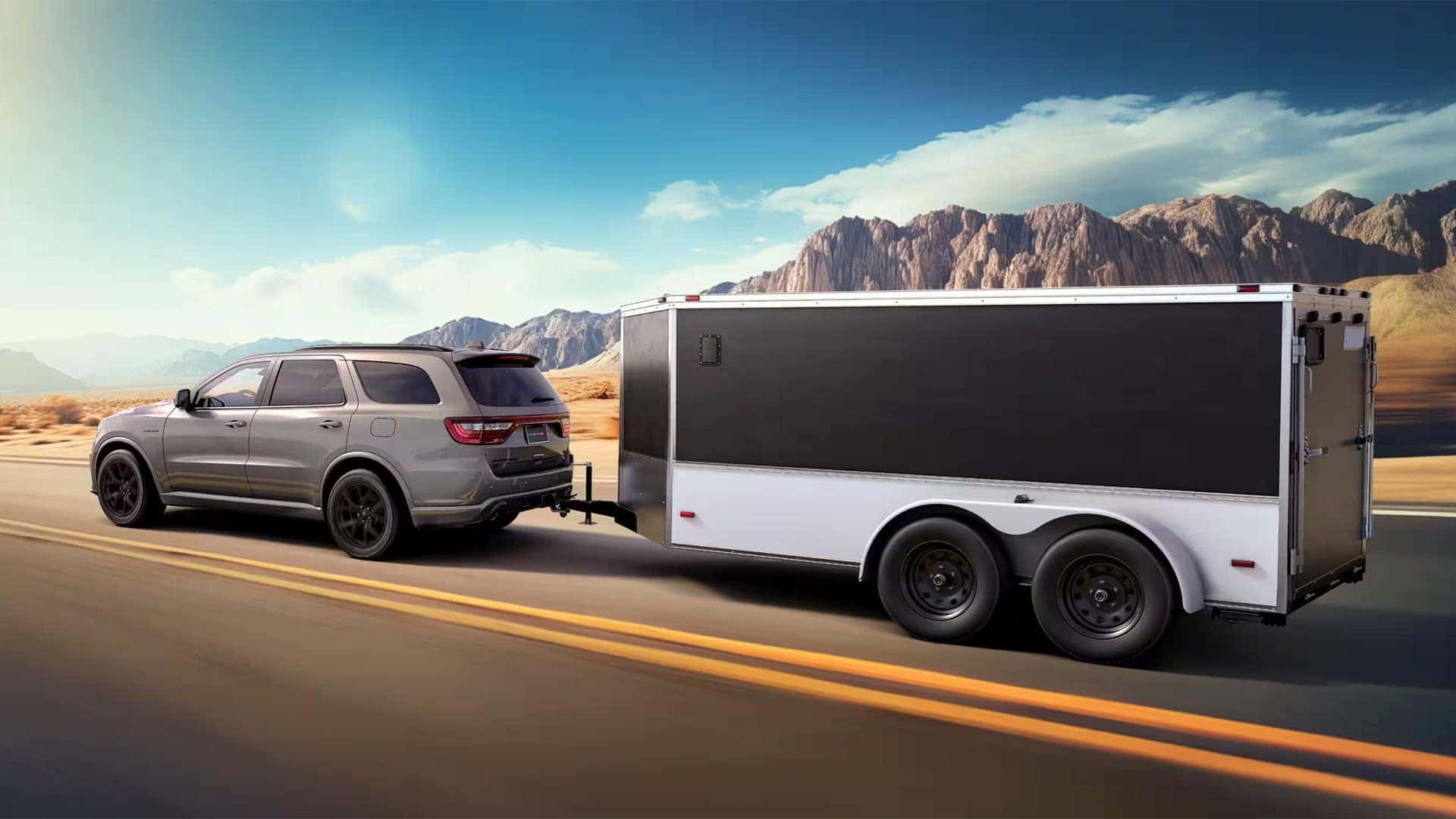 Gray 2026 Dodge Durango towing a large enclosed trailer on a desert highway to demonstrate SUV towing capability.