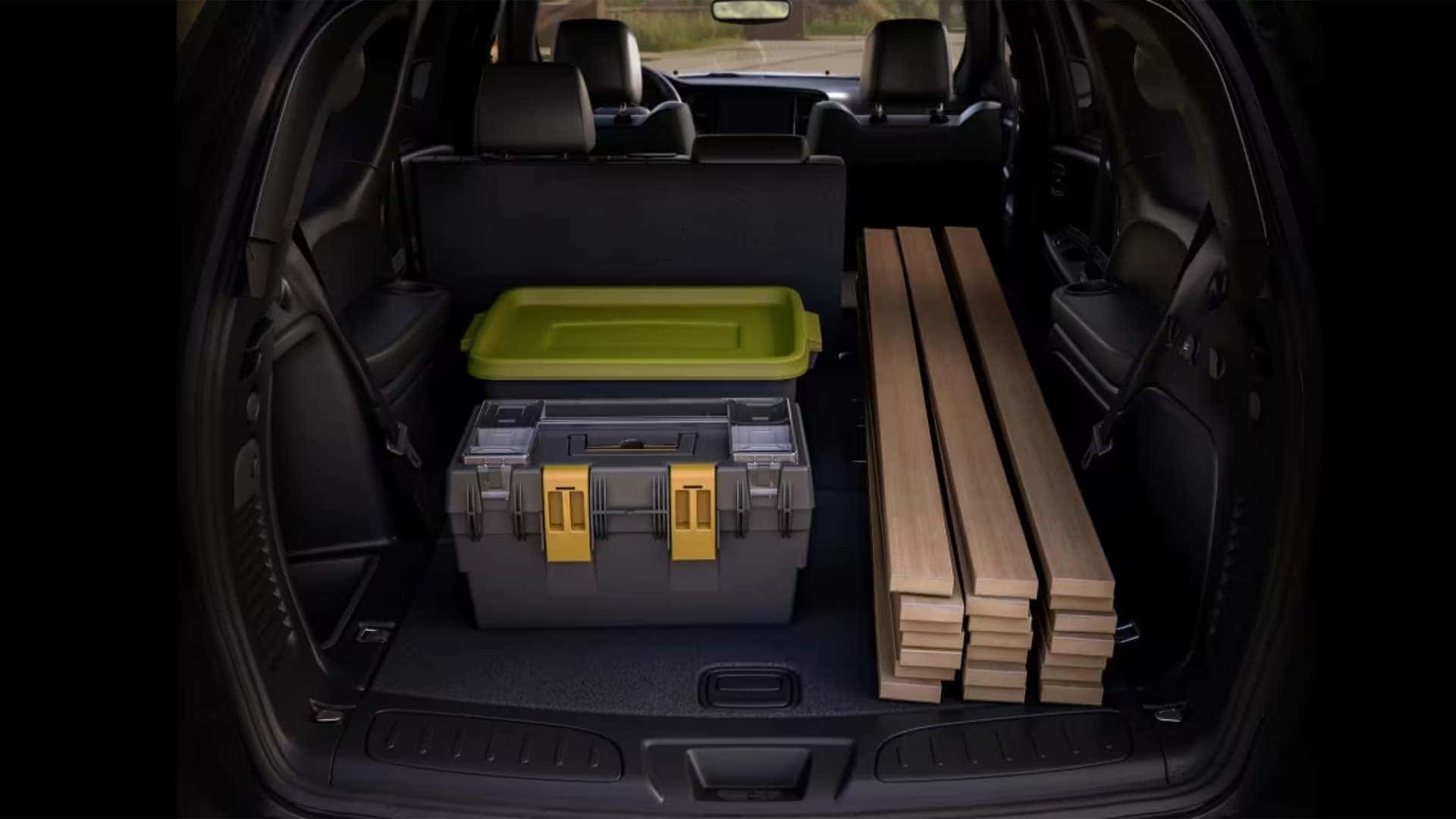 2026 Dodge Durango cargo area with rear seats folded down, showing large storage space carrying tools, storage bins, and wood planks