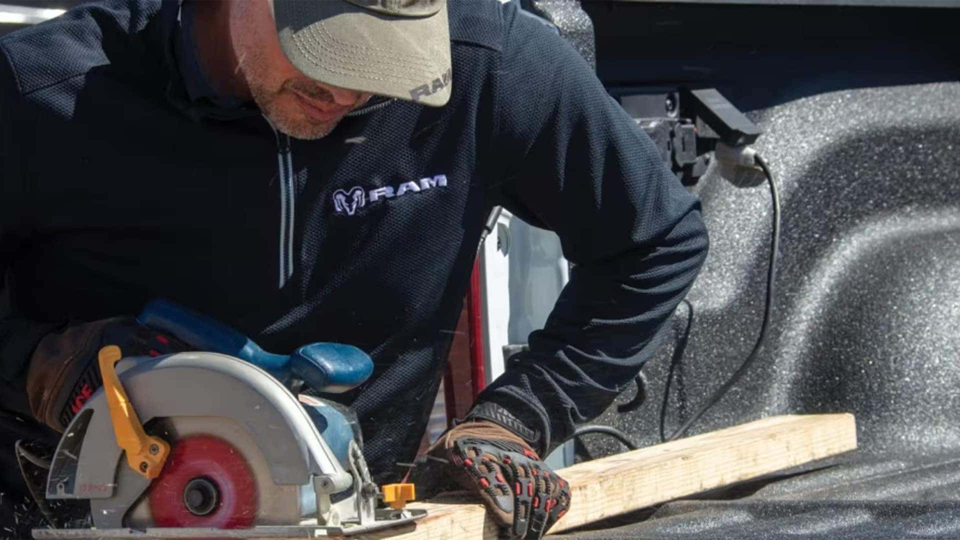 Worker using a circular saw on lumber in the bed of a 2026 RAM 2500 pickup highlighting truck bed durability and work utility