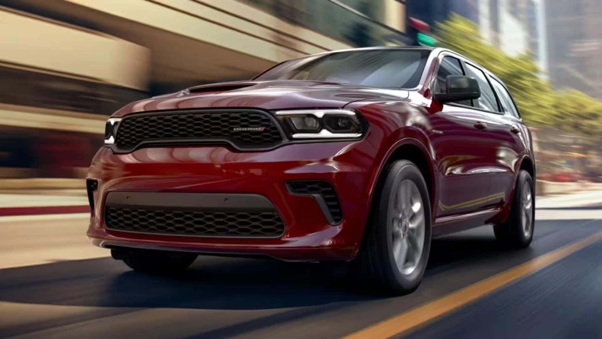 Red 2026 Dodge Durango performance SUV driving quickly through a city street, front view emphasizing sporty grille and muscular design