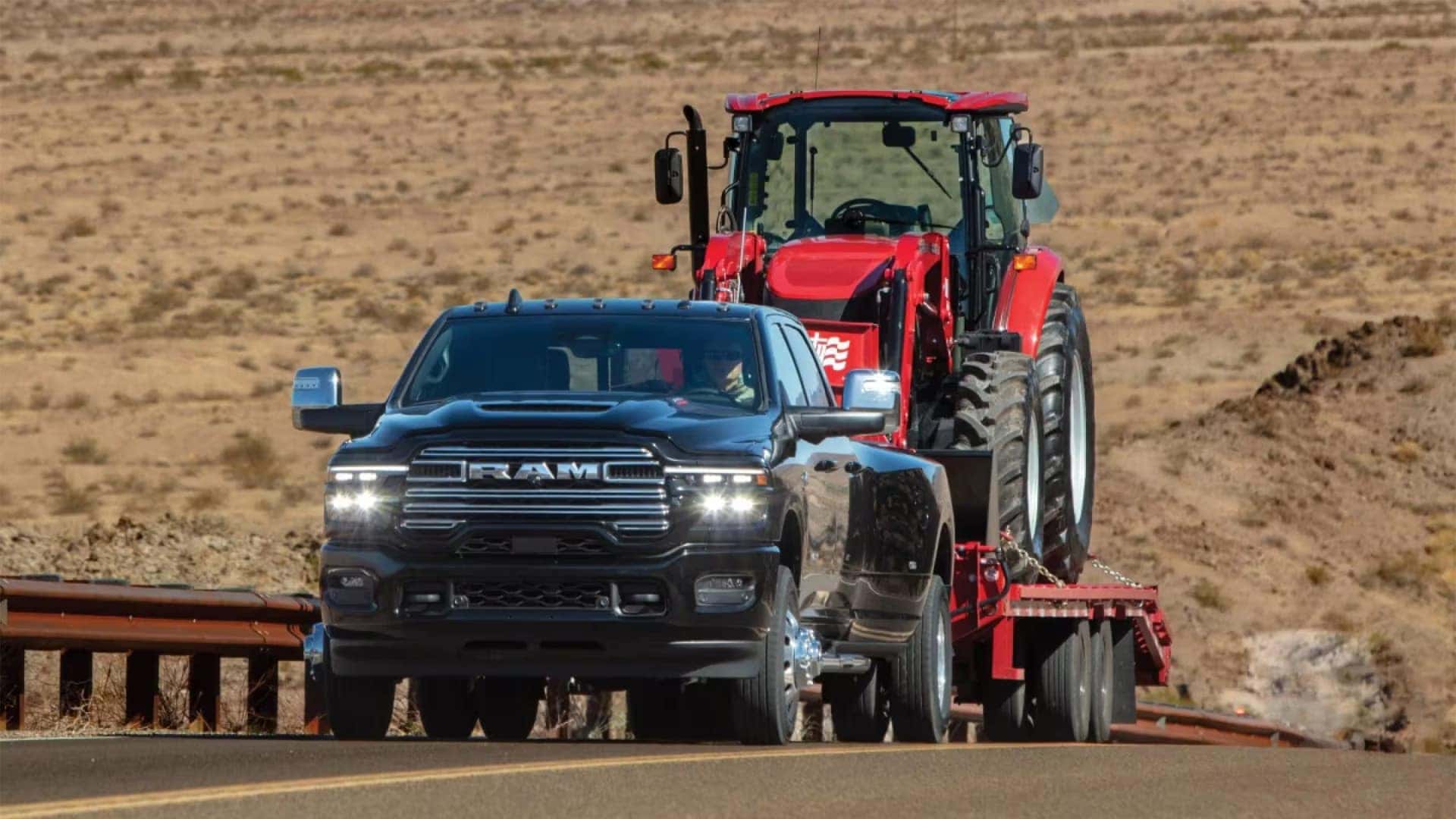 2026 Ram 3500 towing a red tractor on a flatbed trailer across an open road