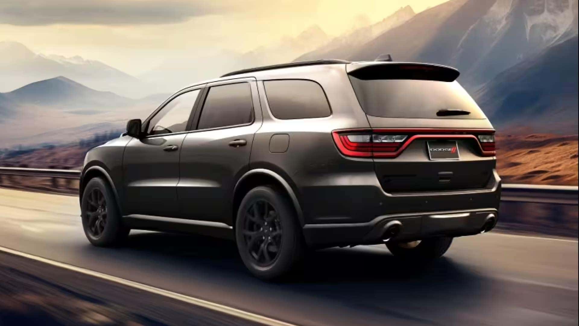 Rear three quarter view of the 2026 Dodge Durango driving on a mountain road showing LED taillights and athletic SUV styling