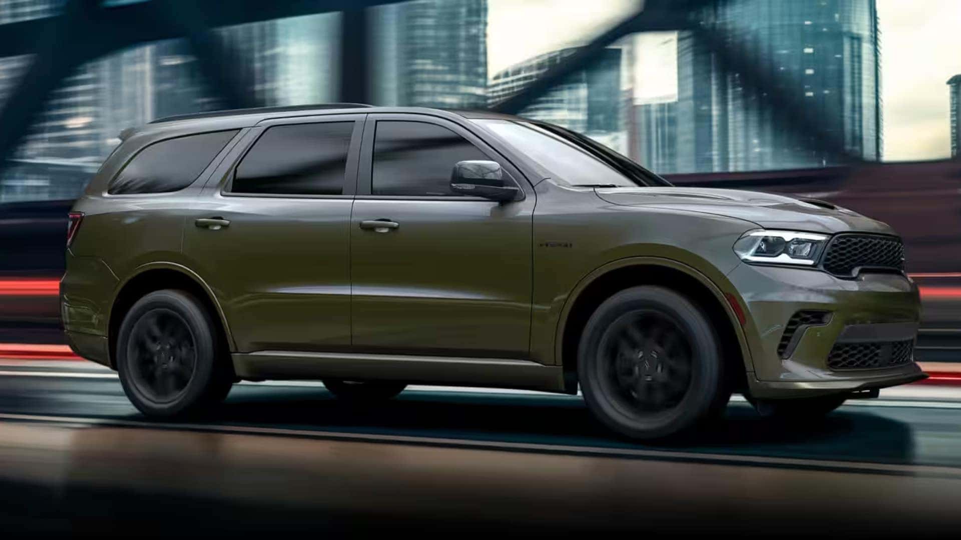 Side profile of a 2026 Dodge Durango SUV driving at speed through an urban setting, highlighting strong stance and three row SUV design