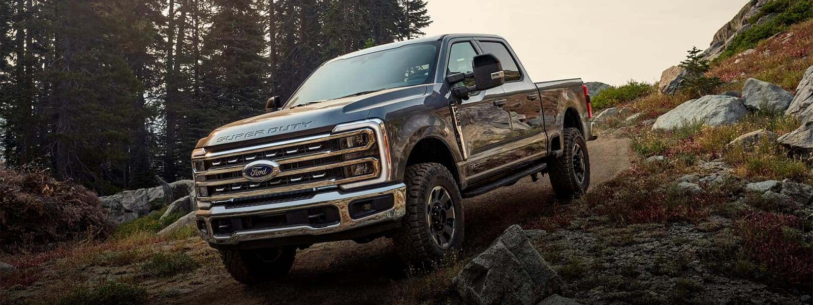 2026 Ford F-350 Super Duty driving on a rocky forest trail, showing front grille, LED lighting, and off-road truck stance