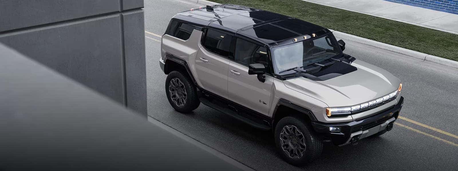 2026 GMC HUMMER EV SUV driving on a city street from an elevated angle, showing bold electric SUV design and roof details