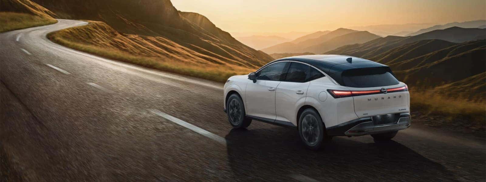2026 Nissan Murano driving on a winding mountain road at sunset, rear three quarter view