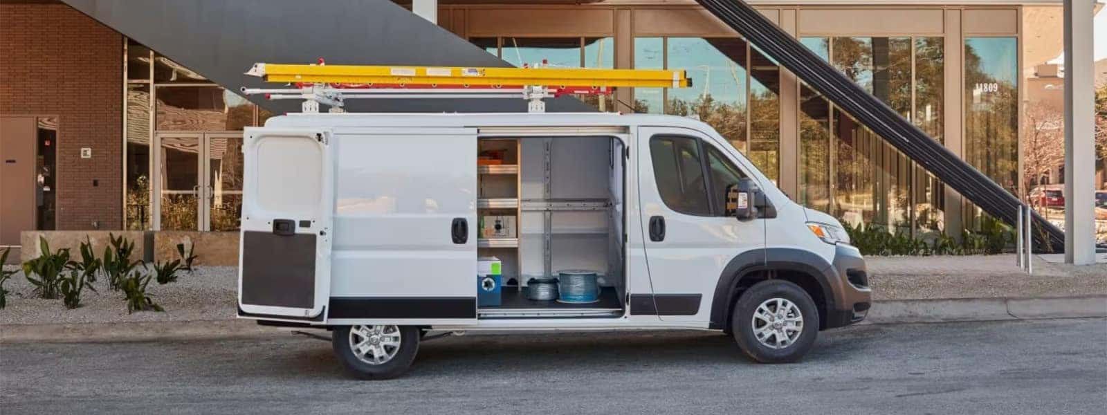 2026 RAM ProMaster Cargo Van with ladder rack and open side door parked at a commercial building