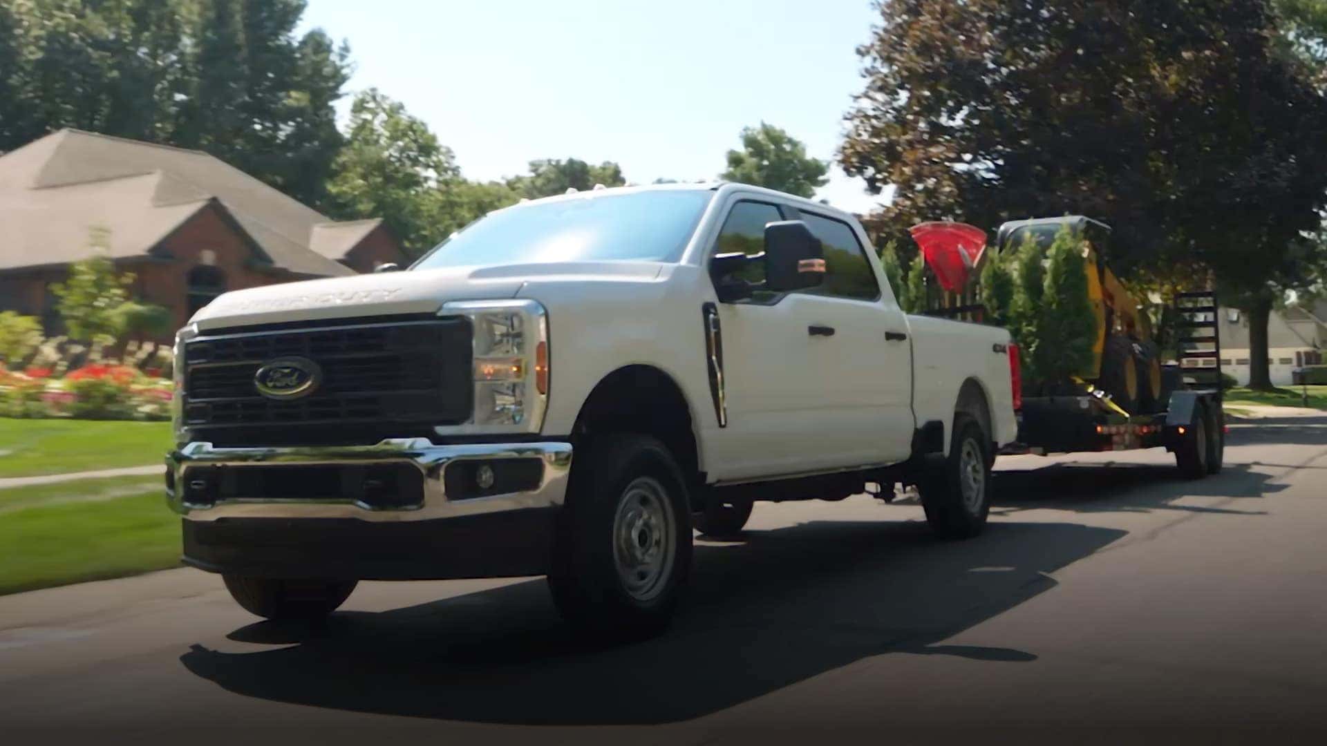 2026 Ford F-350 Super Duty towing heavy equipment on a utility trailer through a residential area