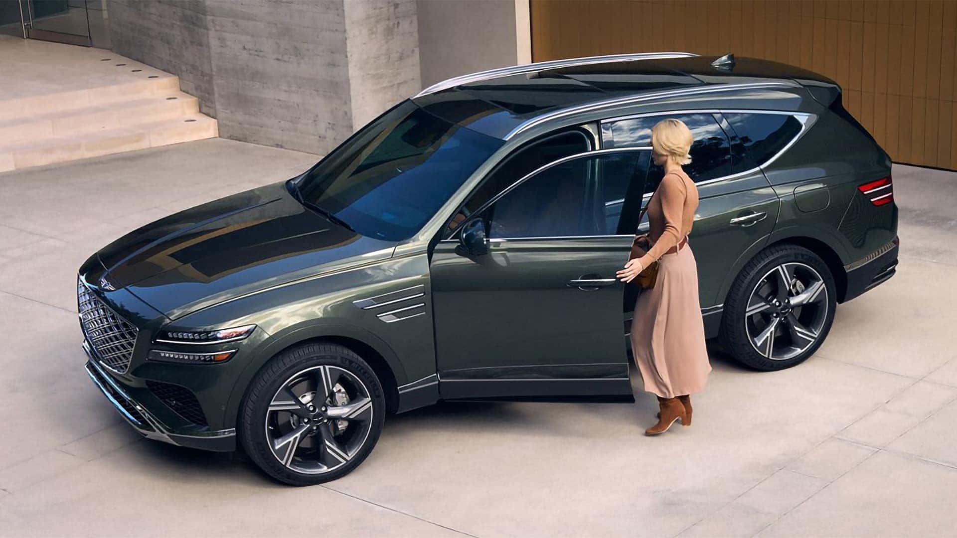 2026 Genesis GV80 parked outside a modern home showing front grille, LED headlights, and large alloy wheels