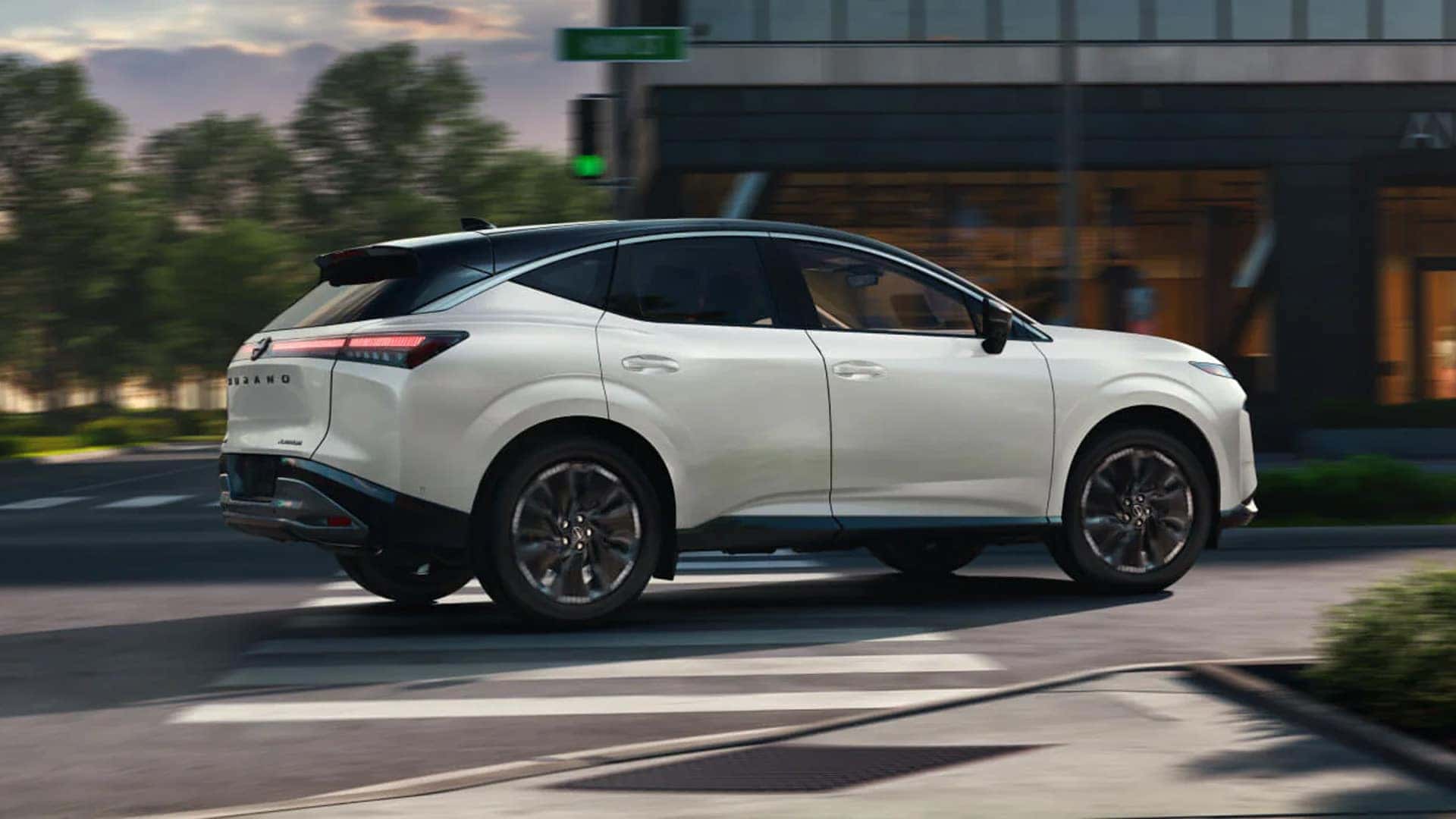 White 2026 Nissan Murano driving through a city street, showing rear three quarter exterior design