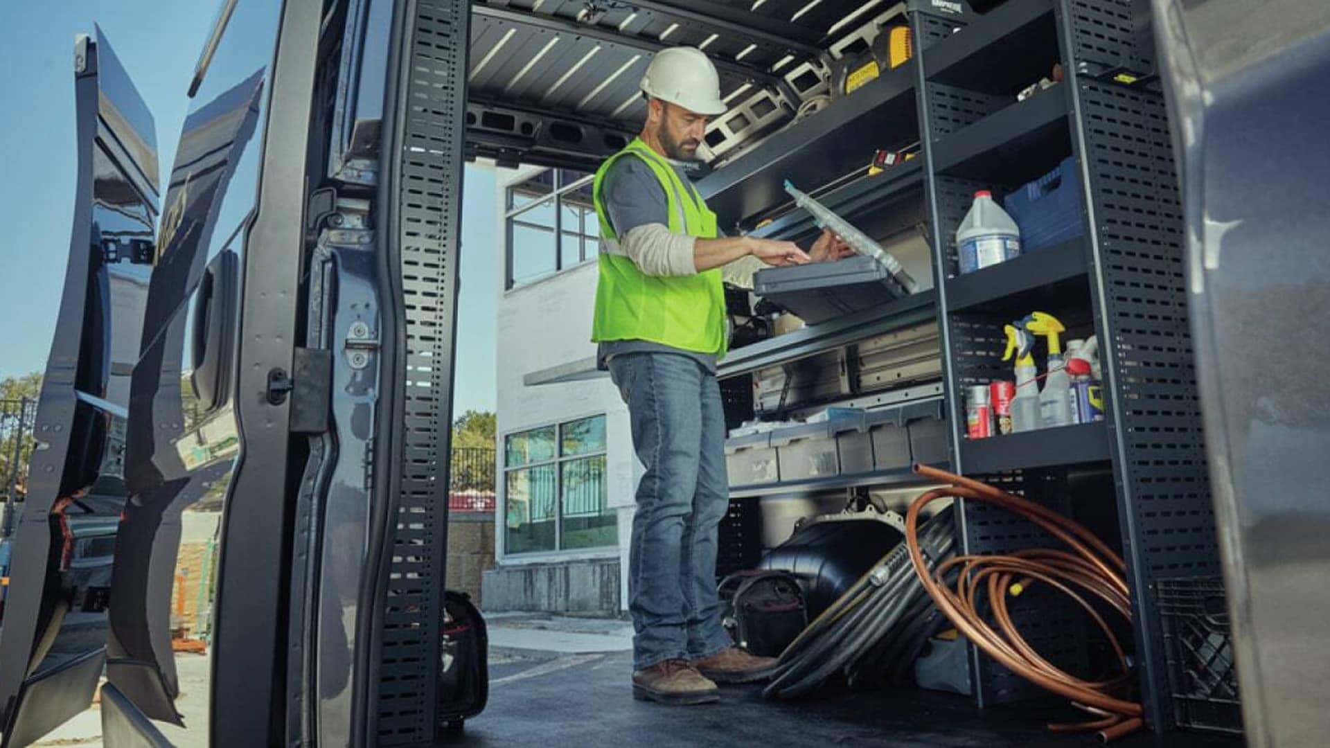Worker organizing tools and equipment inside a 2026 RAM ProMaster Cargo Van with built-in shelving